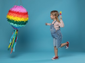 Photo of Happy girl with bright pinata and stick on light blue background