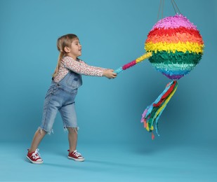 Photo of Happy girl breaking bright pinata with stick on light blue background