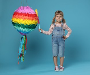 Photo of Cute girl with bright pinata and stick on light blue background