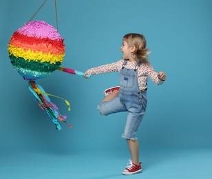 Happy girl breaking bright pinata with stick on light blue background