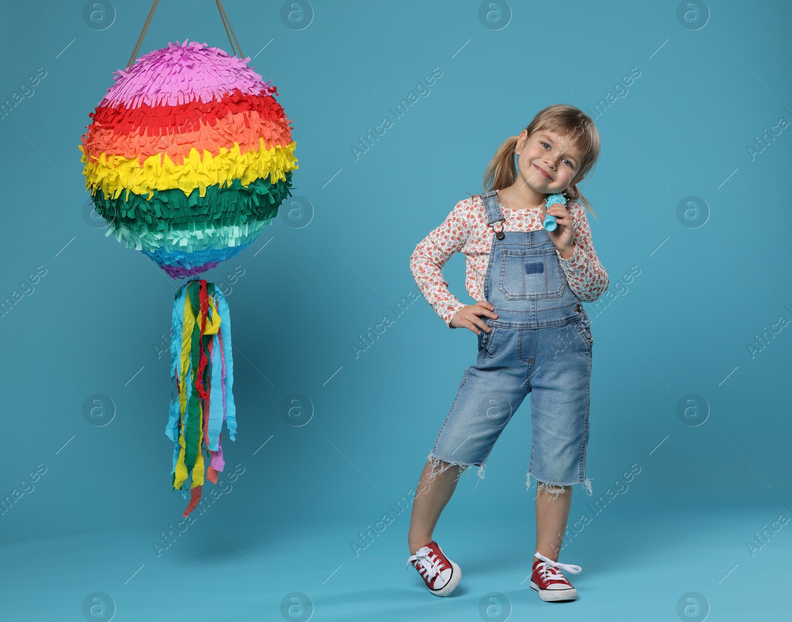 Photo of Cute girl with bright pinata and stick on light blue background