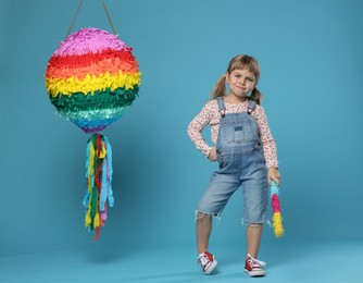 Cute girl with bright pinata and stick on light blue background