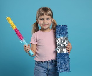 Happy girl with bright pinata and stick on light blue background