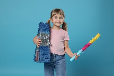 Photo of Cute girl with bright pinata and stick on light blue background