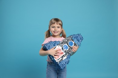 Photo of Happy girl with rocket shaped pinata on light blue background