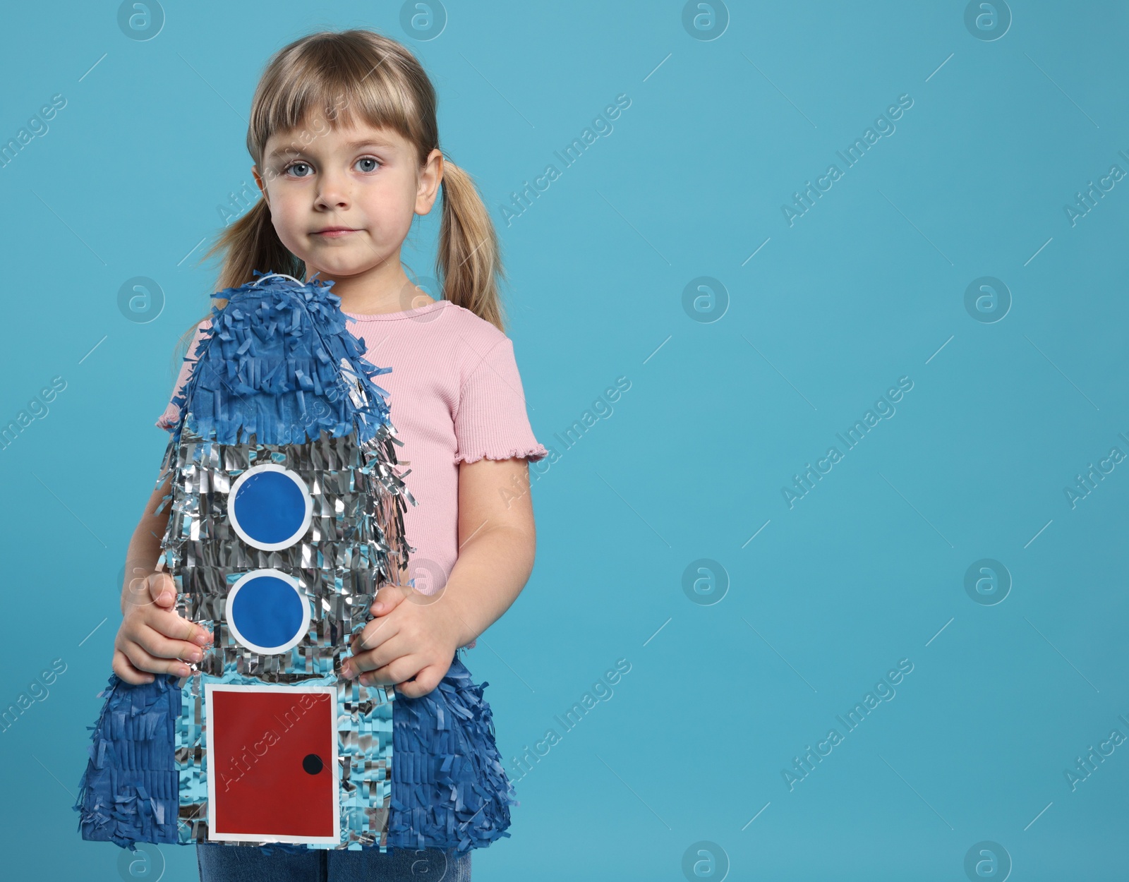 Photo of Cute girl with rocket shaped pinata on light blue background. Space for text