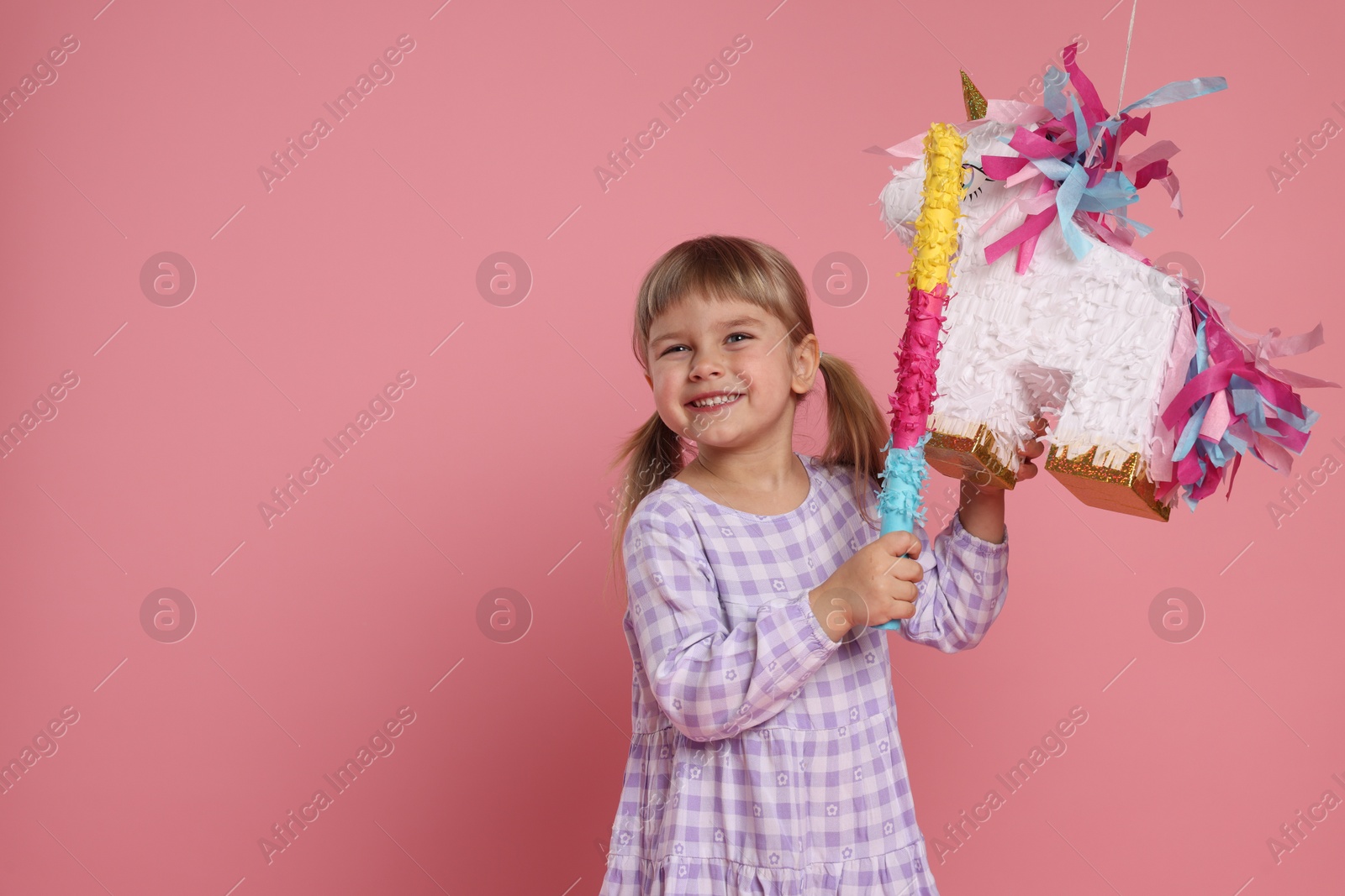 Photo of Happy girl with unicorn shaped pinata and stick on pink background. Space for text