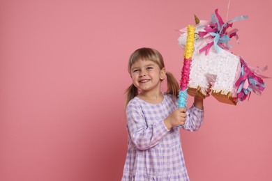 Photo of Happy girl with unicorn shaped pinata and stick on pink background. Space for text