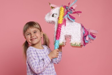 Happy girl with unicorn shaped pinata and stick on pink background