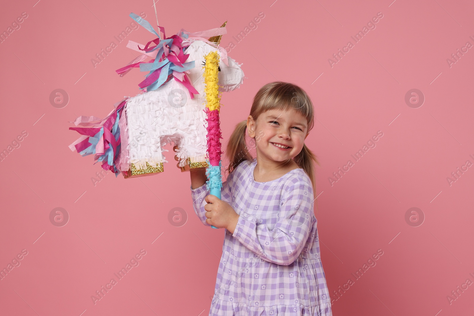 Photo of Happy girl with unicorn shaped pinata and stick on pink background