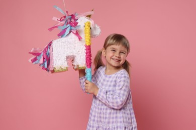 Happy girl with unicorn shaped pinata and stick on pink background