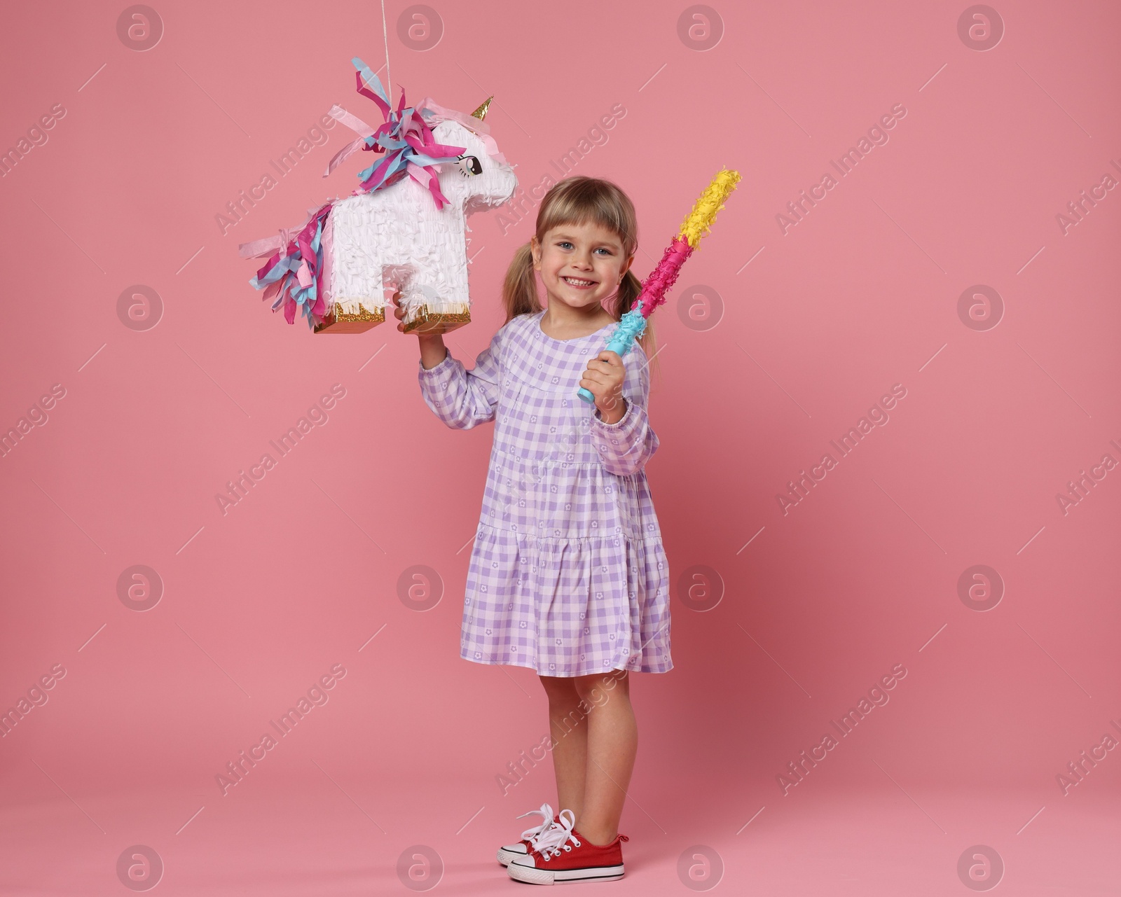 Photo of Happy girl with unicorn shaped pinata and stick on pink background