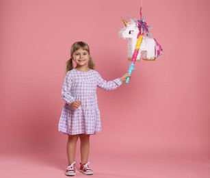 Photo of Happy girl with unicorn shaped pinata and stick on pink background