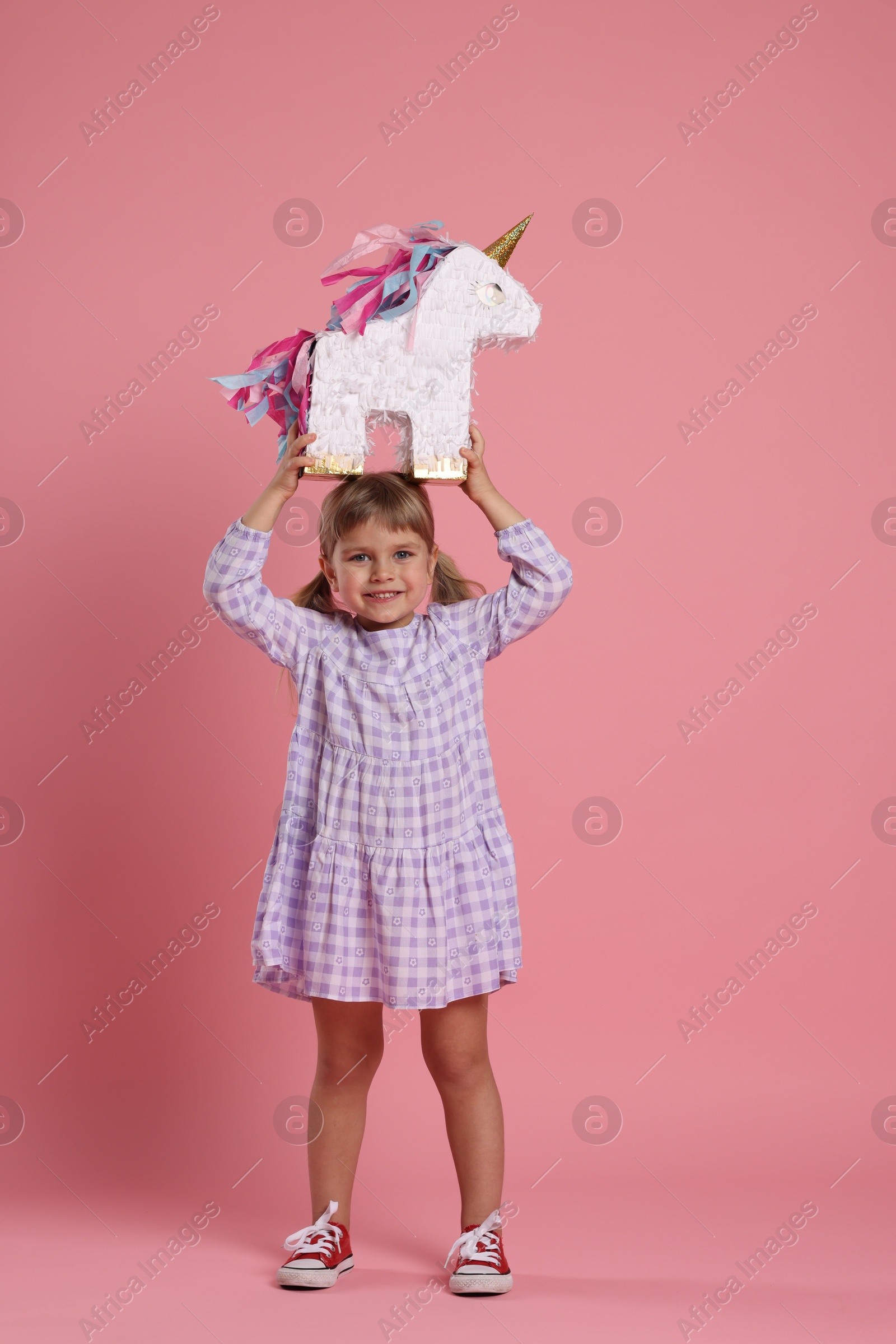 Photo of Happy girl with unicorn shaped pinata on pink background