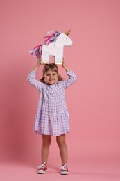 Happy girl with unicorn shaped pinata on pink background