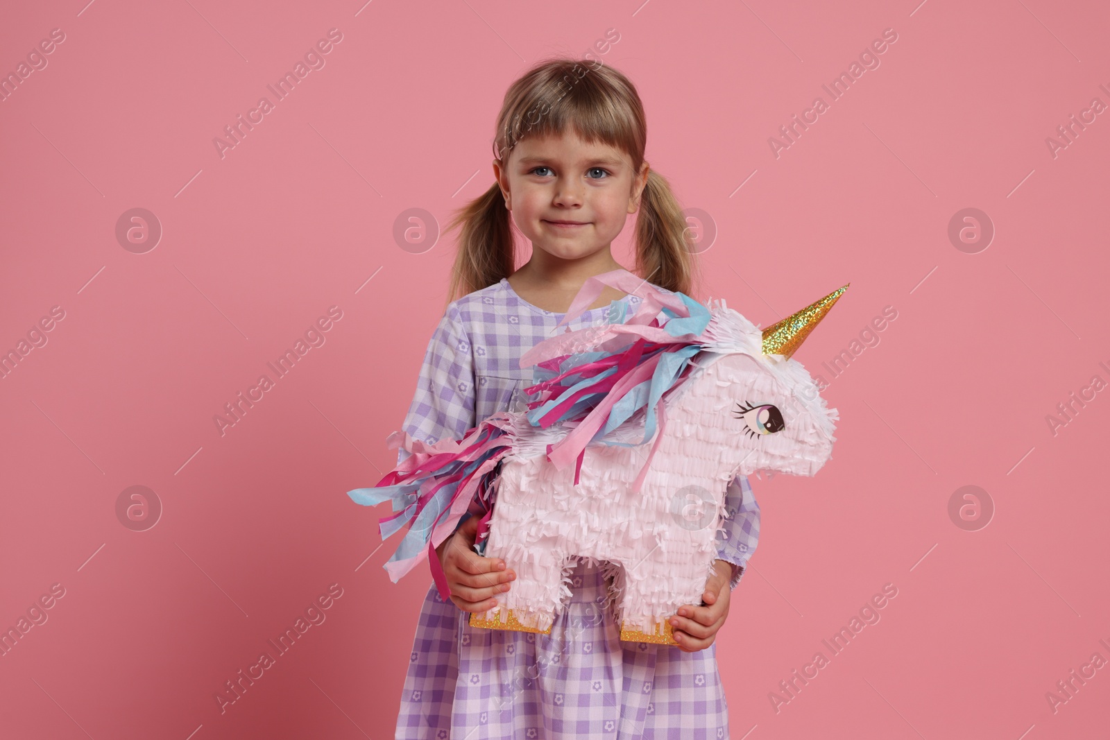 Photo of Cute girl with unicorn shaped pinata on pink background