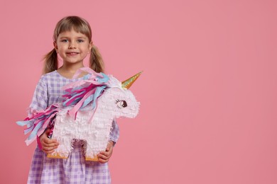 Photo of Happy girl with unicorn shaped pinata on pink background. Space for text