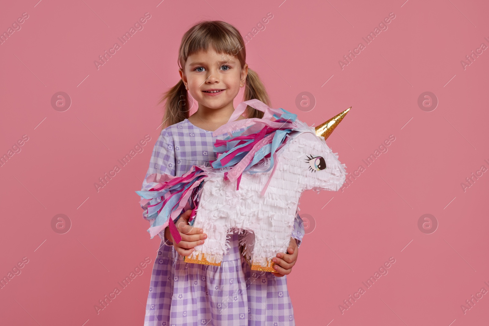 Photo of Happy girl with unicorn shaped pinata on pink background