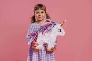 Happy girl with unicorn shaped pinata on pink background