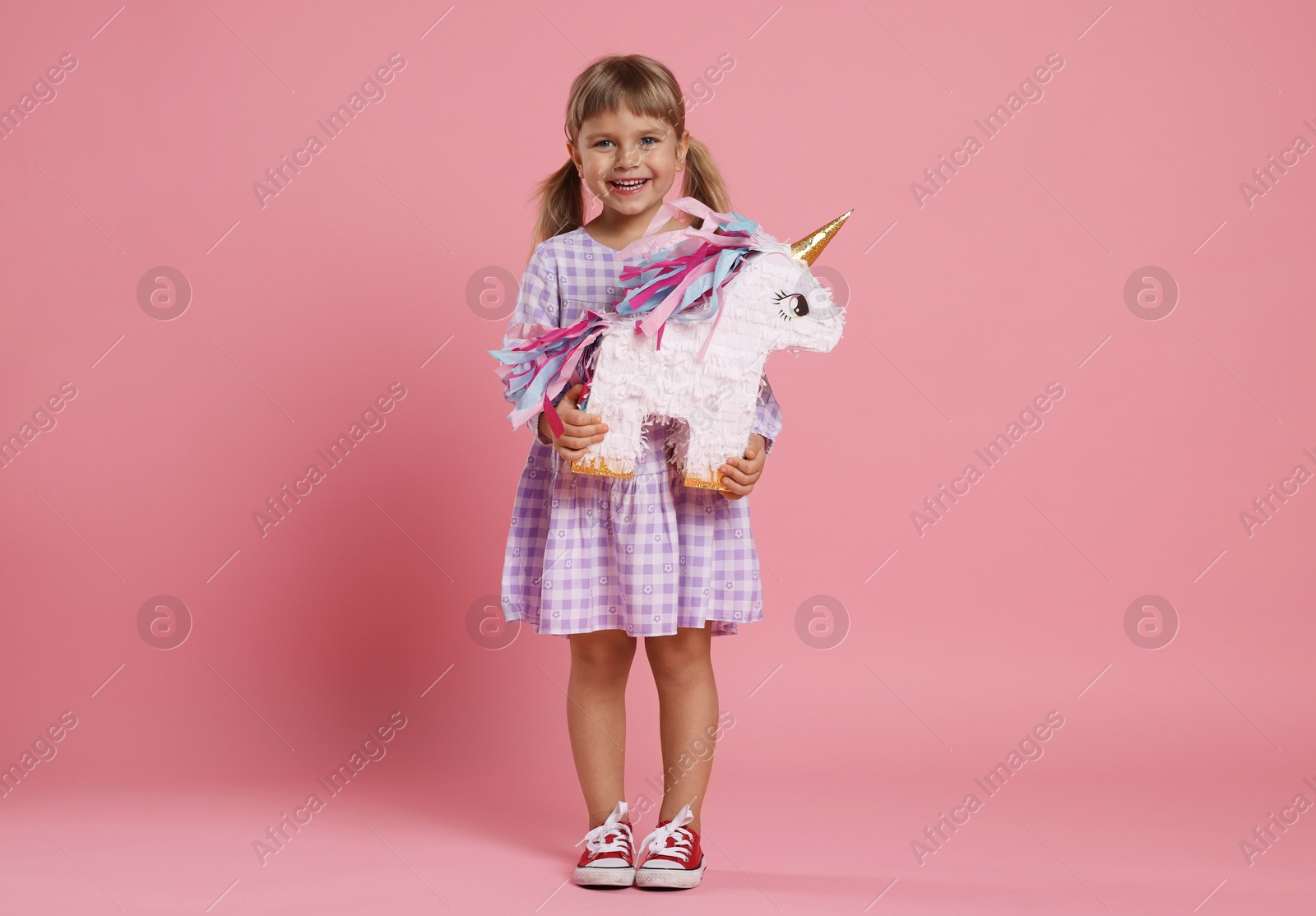 Photo of Happy girl with unicorn shaped pinata on pink background