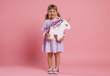 Photo of Happy girl with unicorn shaped pinata on pink background