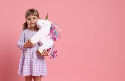 Photo of Cute girl with unicorn shaped pinata on pink background. Space for text