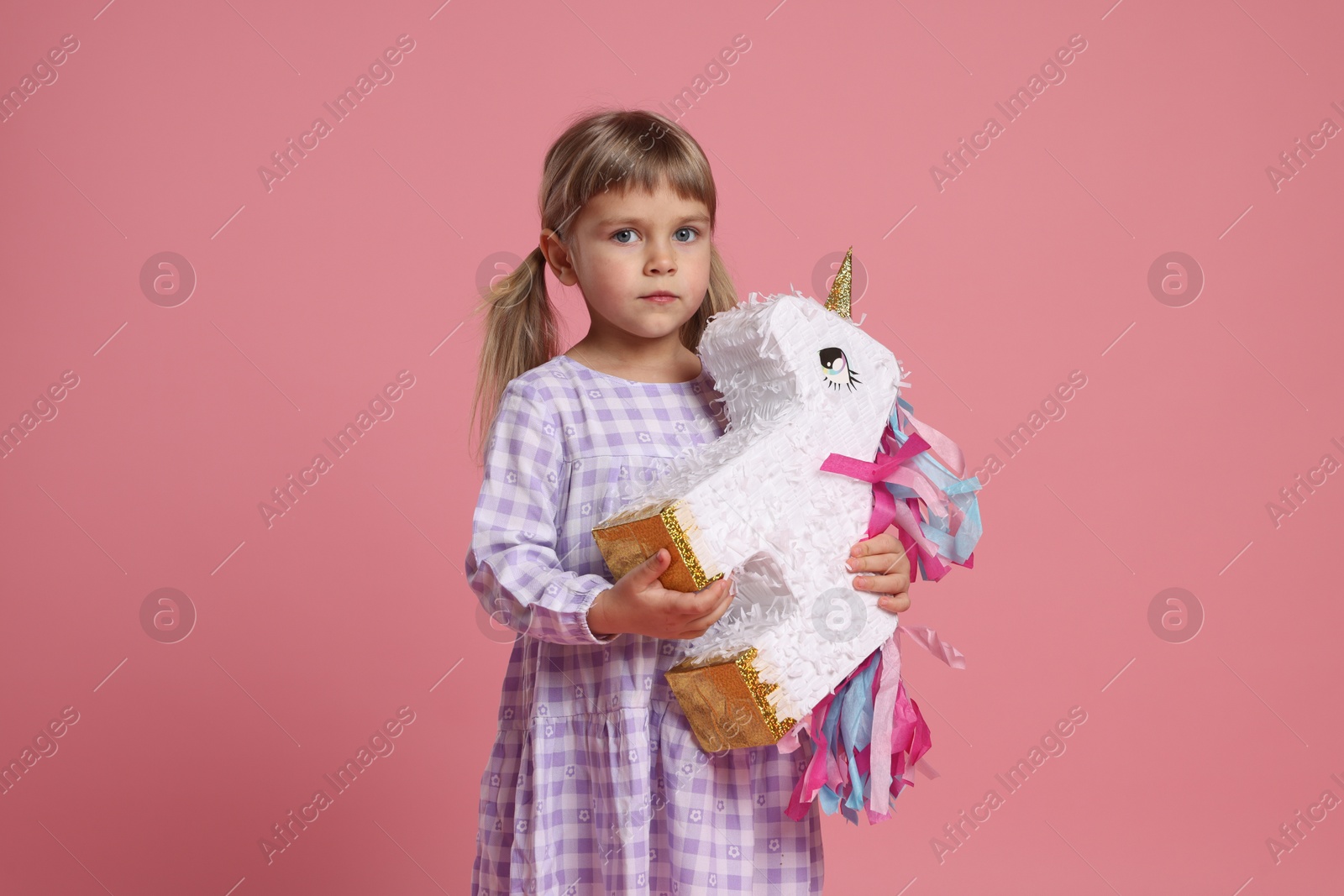 Photo of Cute girl with unicorn shaped pinata on pink background