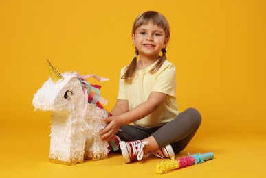 Photo of Happy girl with unicorn shaped pinata and stick on orange background