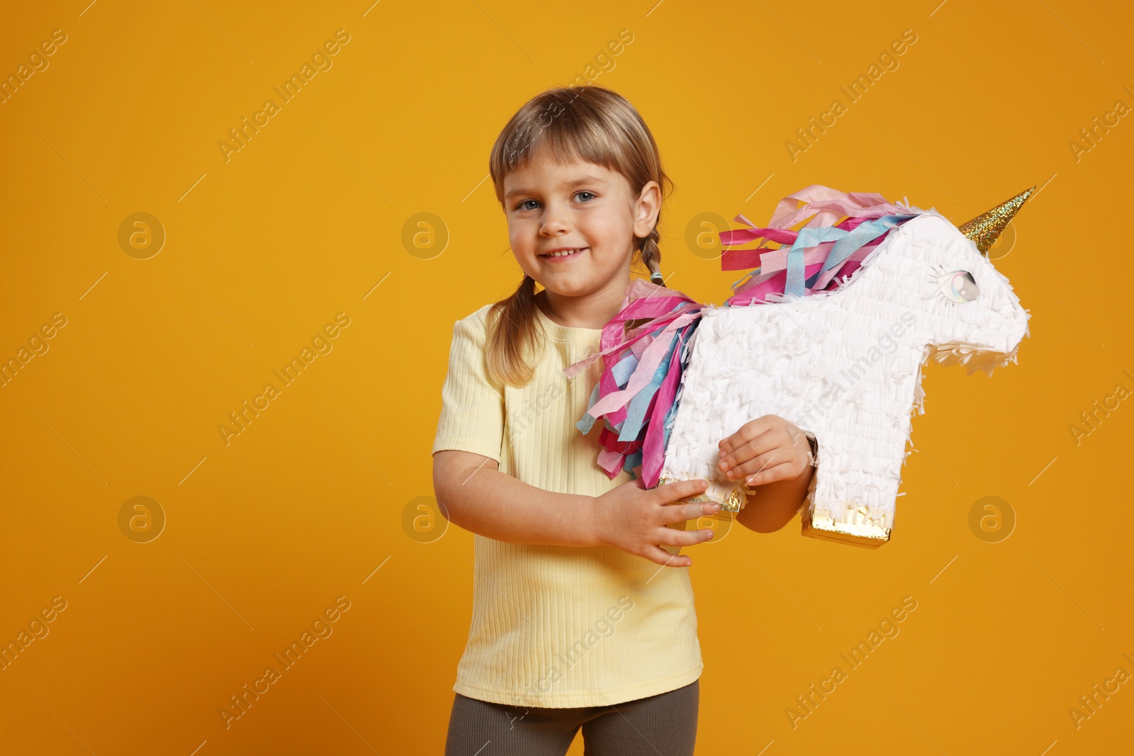 Photo of Happy girl with unicorn shaped pinata on orange background. Space for text