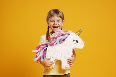 Photo of Happy girl with unicorn shaped pinata on orange background