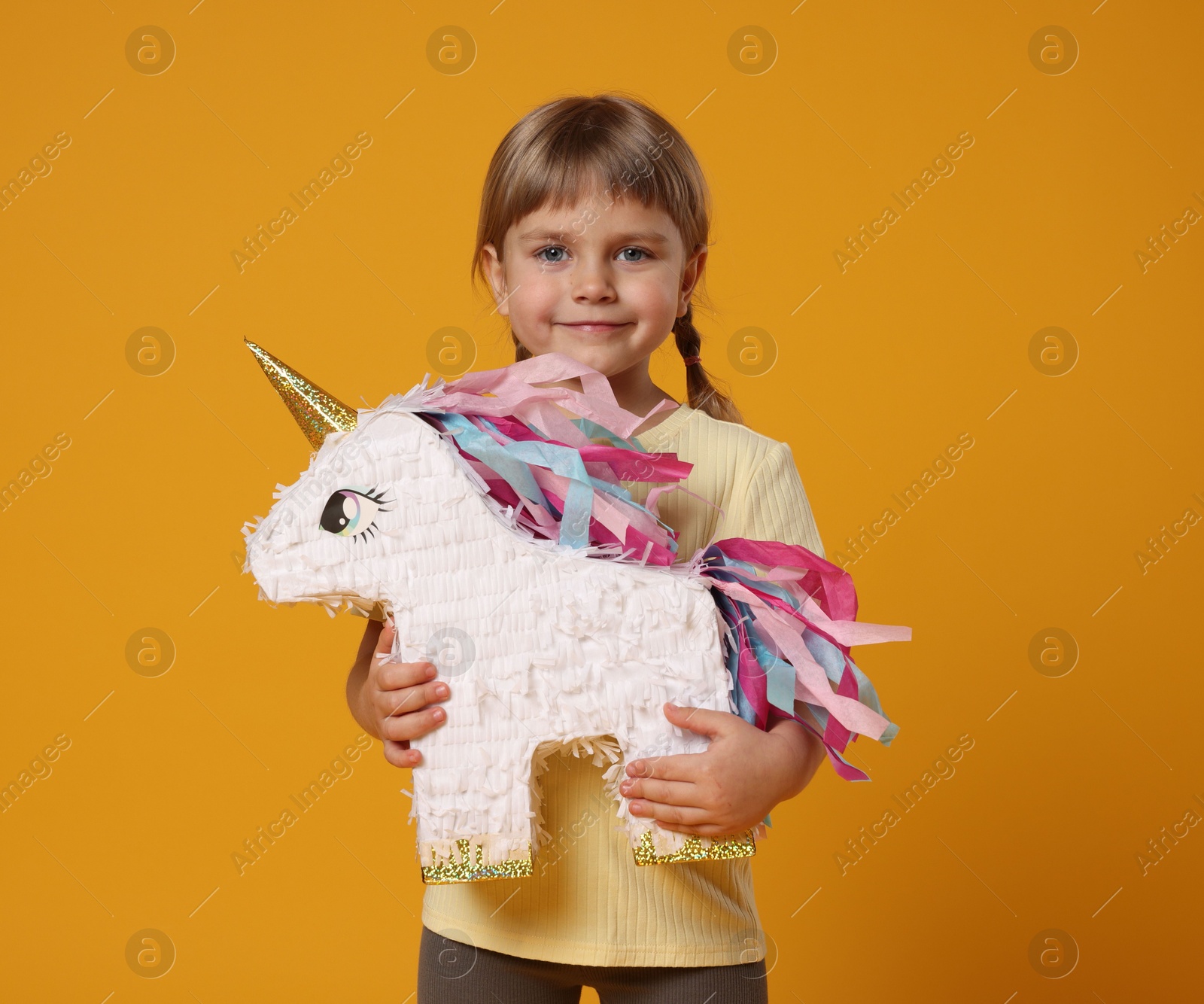 Photo of Cute girl with unicorn shaped pinata on orange background