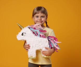 Cute girl with unicorn shaped pinata on orange background