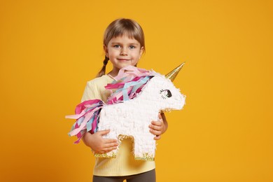 Cute girl with unicorn shaped pinata on orange background