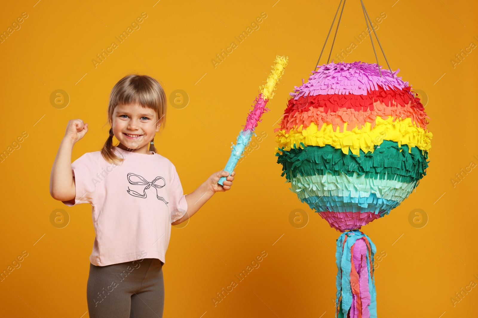 Photo of Happy girl with bright pinata and stick on orange background