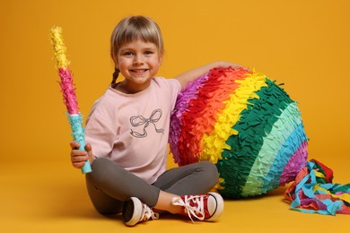 Photo of Happy girl with bright pinata and stick on orange background