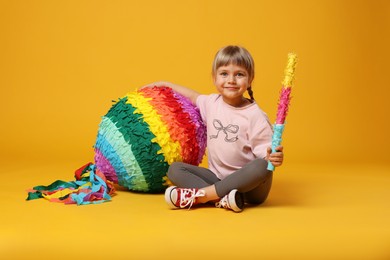 Cute girl with bright pinata and stick on orange background