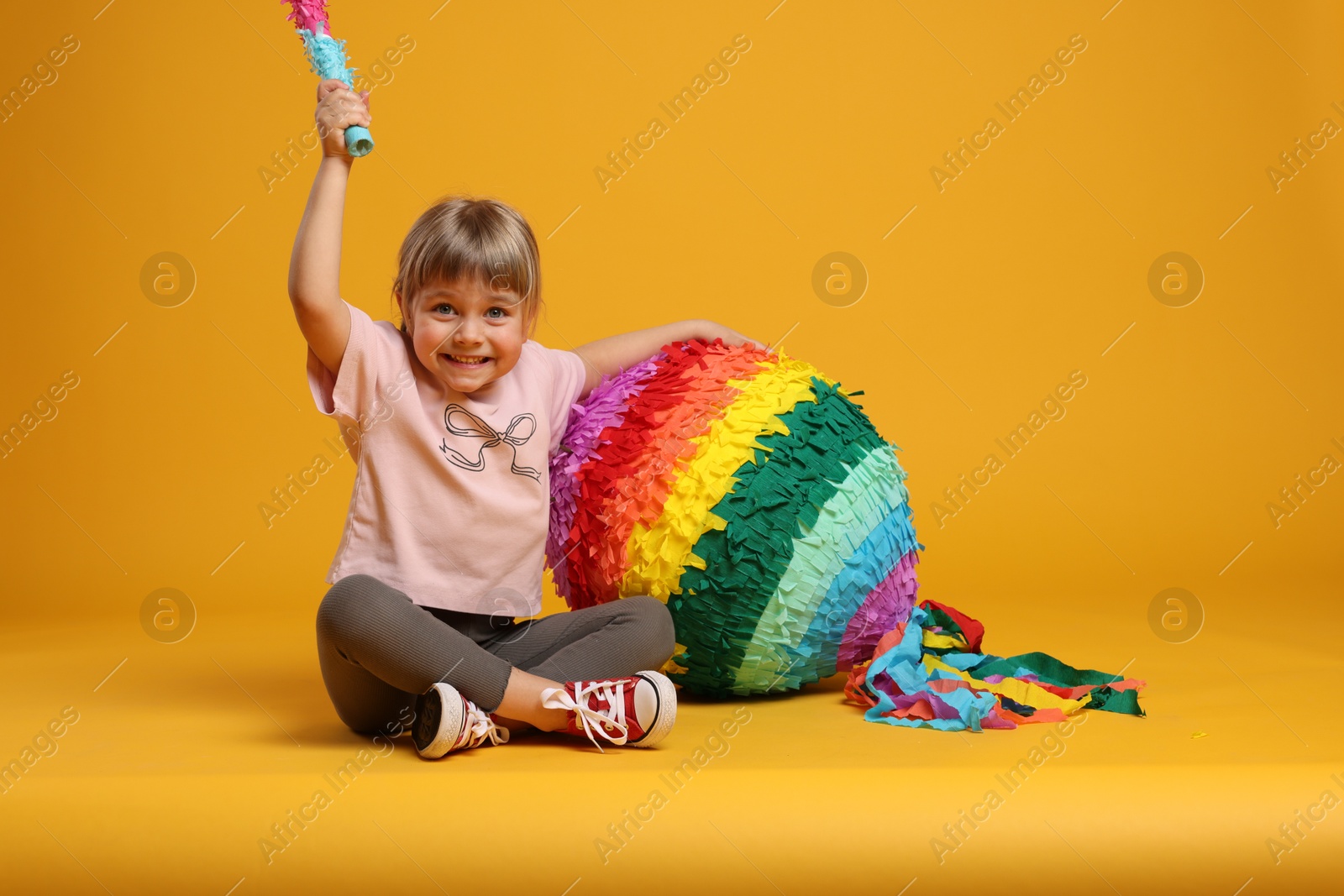 Photo of Happy girl with bright pinata and stick on orange background