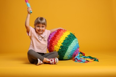 Photo of Happy girl with bright pinata and stick on orange background