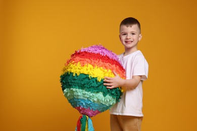 Happy boy with bright pinata on orange background