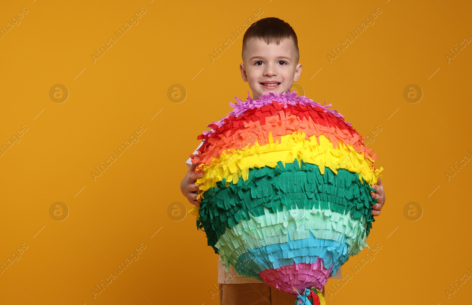 Photo of Happy boy with bright pinata on orange background. Space for text