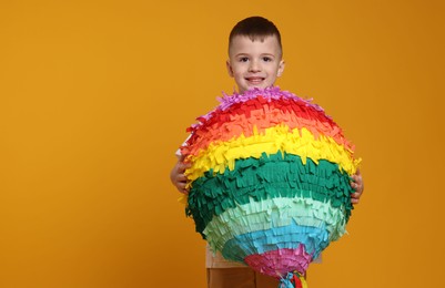 Photo of Happy boy with bright pinata on orange background. Space for text