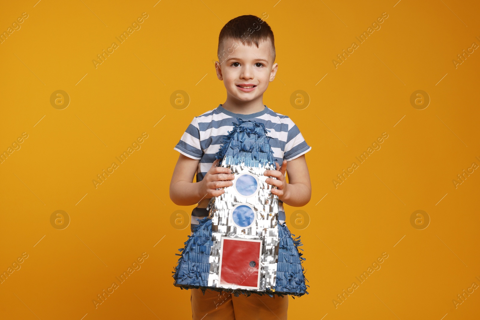 Photo of Happy boy with rocket shaped pinata on orange background