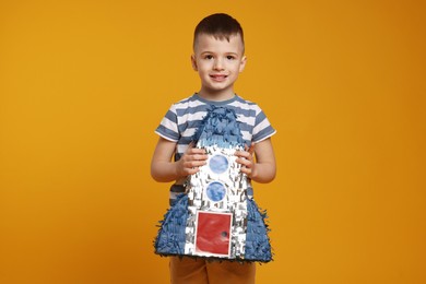 Photo of Happy boy with rocket shaped pinata on orange background