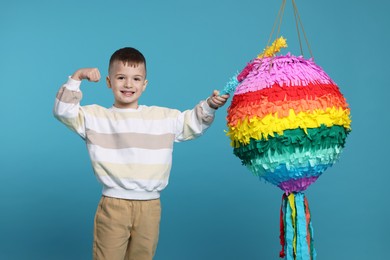 Happy boy with bright pinata and stick on light blue background