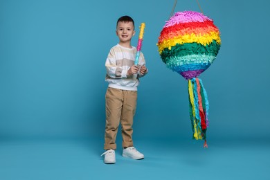 Happy boy with bright pinata and stick on light blue background