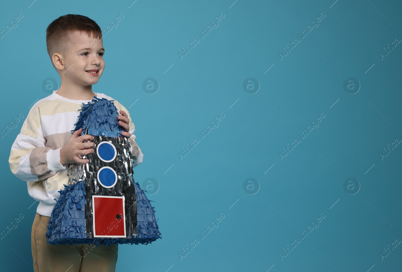 Photo of Happy boy with rocket shaped pinata on light blue background. Space for text