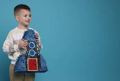 Happy boy with rocket shaped pinata on light blue background. Space for text