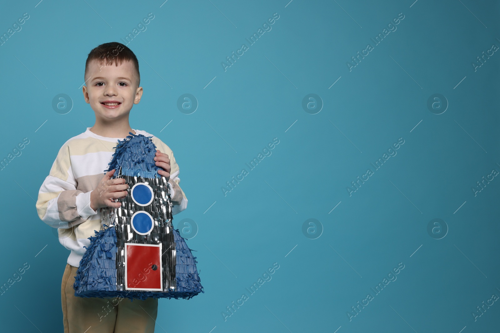 Photo of Happy boy with rocket shaped pinata on light blue background. Space for text