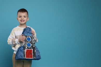 Happy boy with rocket shaped pinata on light blue background. Space for text