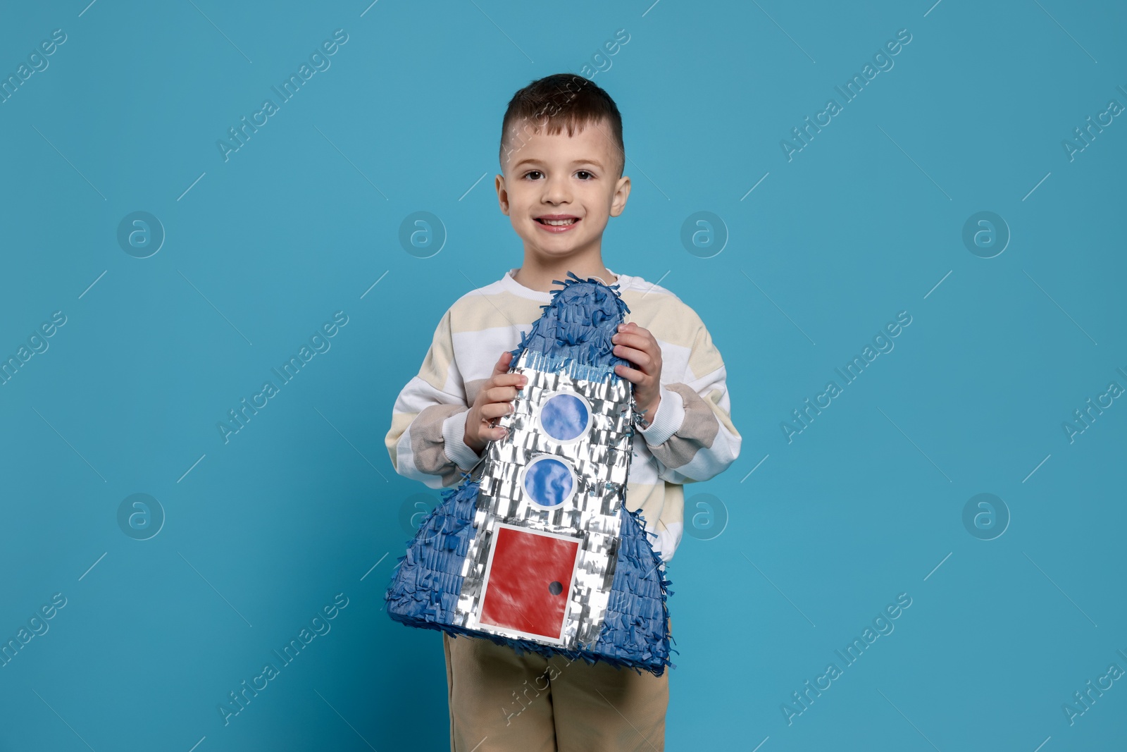 Photo of Happy boy with rocket shaped pinata on light blue background